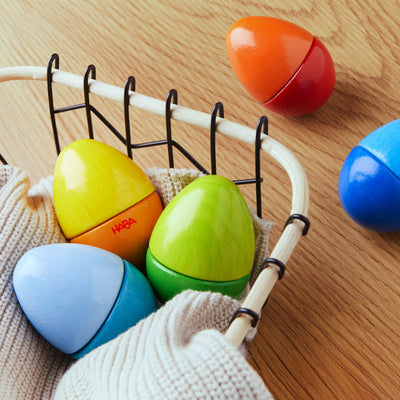 A basket with colorful, wooden egg-shaped toys, and additional eggs on a wooden table.