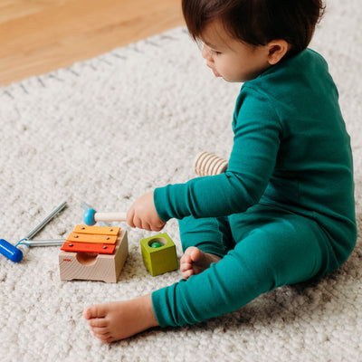 Child in teal onesie playing with a small xylophone on a light textured colored rug.