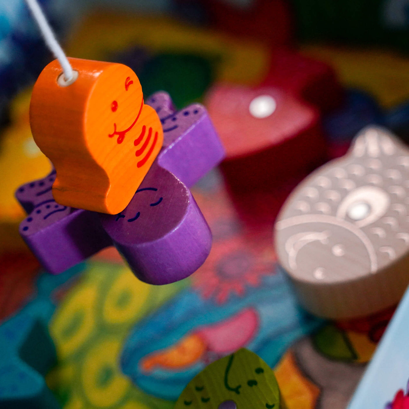 My Very First Games - Here, Fishy, Fishy! Magnetic Game's colorful wooden worm figurine hangs from a fishing line connected to a purple wooden octopus