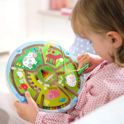 Child playing with a circular farm animal-themed wooden maze with a magnetic wand