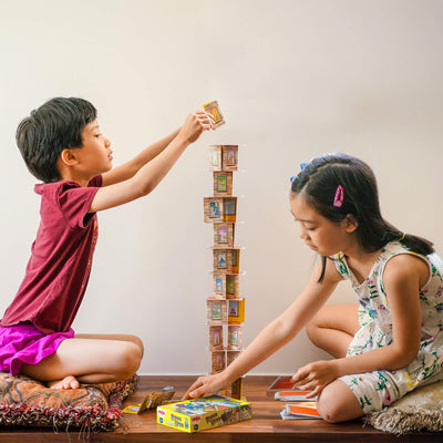 Two children playing a Rhino Hero card stacking game facing each other while sitting on cushions.