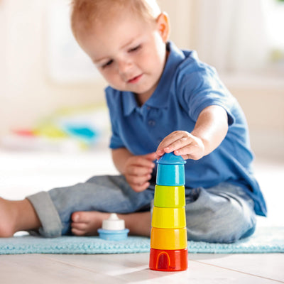 Child sitting on a rug indoors playing with HABA Lighthouse Wooden Rainbow Stacker 