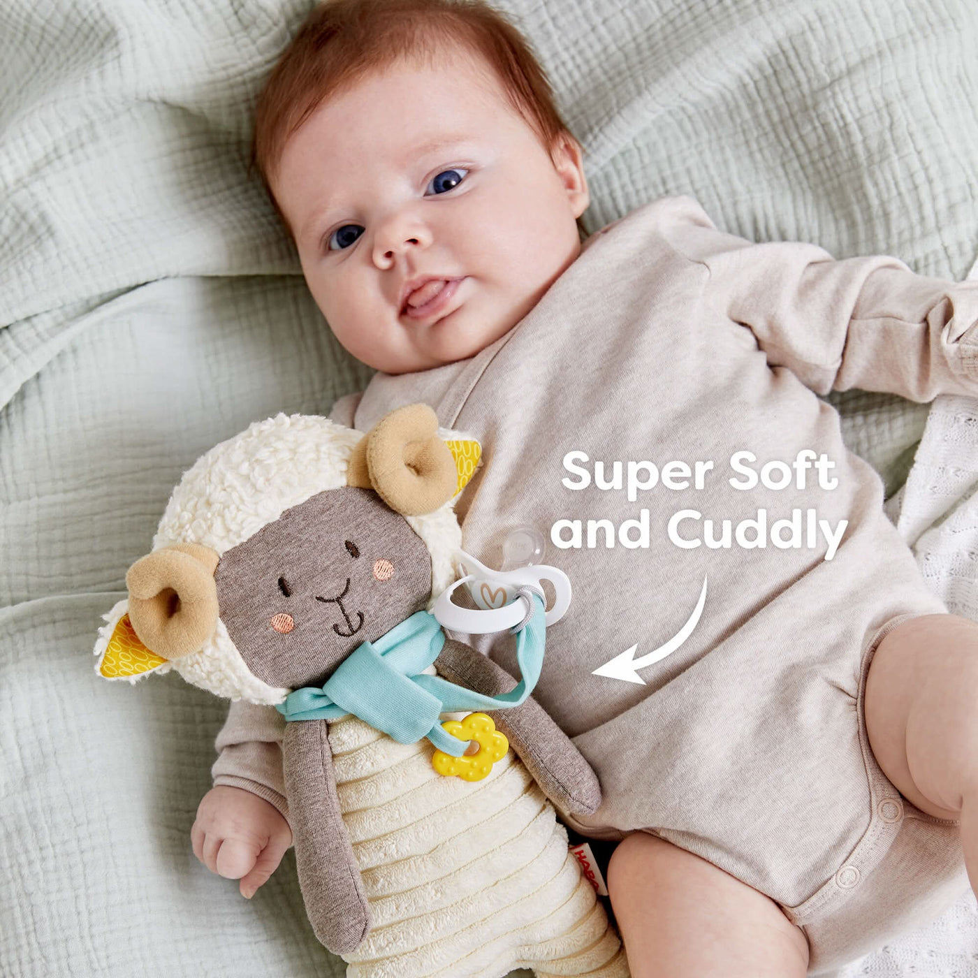 A baby lying on a blanket with a Woolbert the Ram plush toy and text reading "Super Soft and Cuddly."