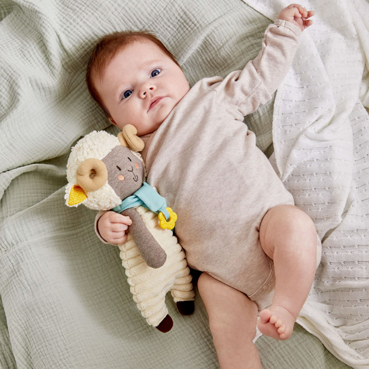 Baby in a beige onesie holding a plush ram toy on a textured green and white blanket.